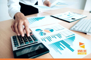 empresario fazendo contas com uma calculadora acima de uma mesa com papeis de graficos